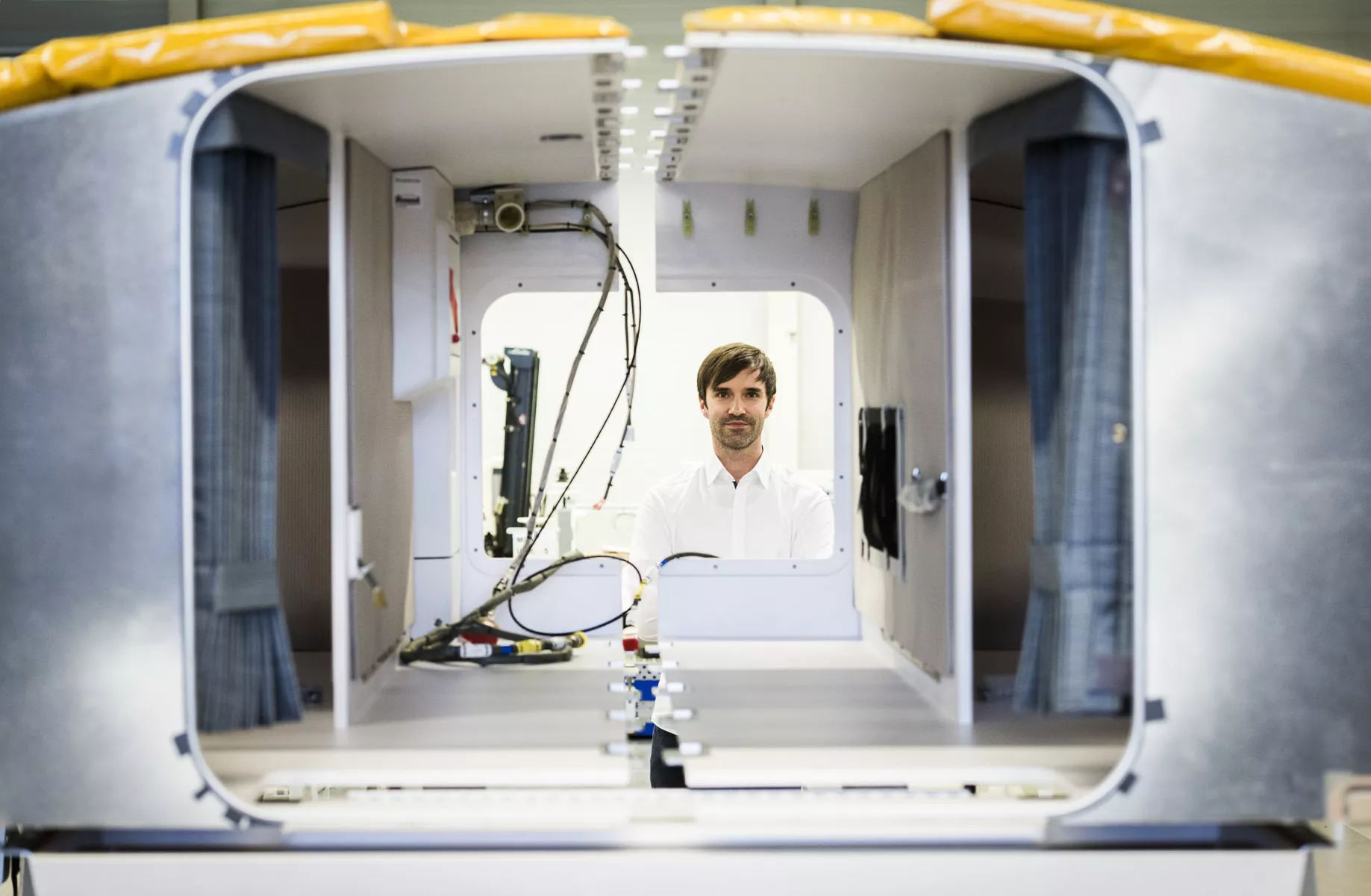 Portrait eines Mitarbeiters mit Blick durch eine Schlafkabine eines Flugzeugs in der Fertigung